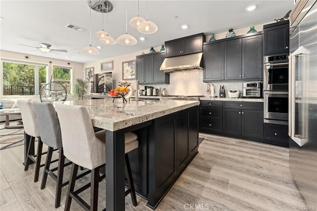 kitchen featuring a spacious island, tasteful backsplash, light hardwood / wood-style floors, hanging light fixtures, and ceiling fan