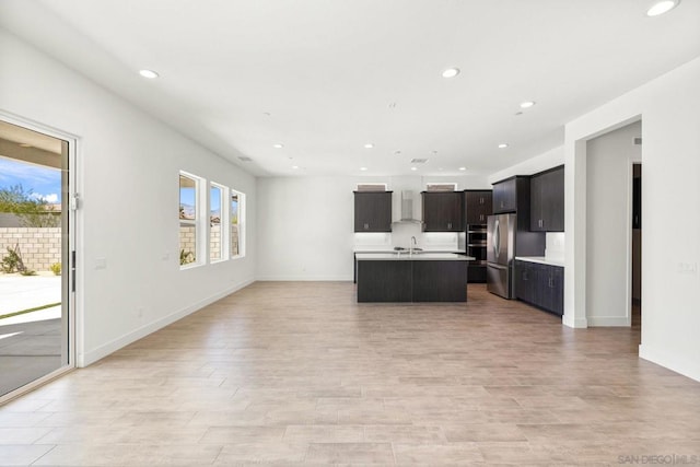 kitchen with light hardwood / wood-style floors, stainless steel fridge, an island with sink, wall chimney range hood, and sink