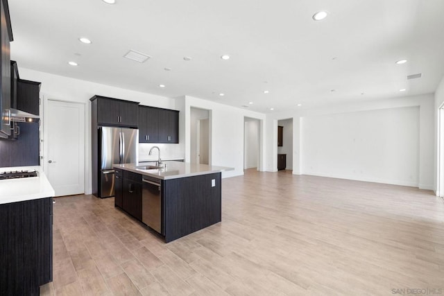 kitchen featuring light wood-type flooring, a kitchen island with sink, appliances with stainless steel finishes, and sink