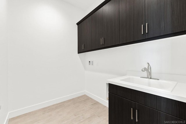 laundry room featuring cabinets, sink, and light wood-type flooring