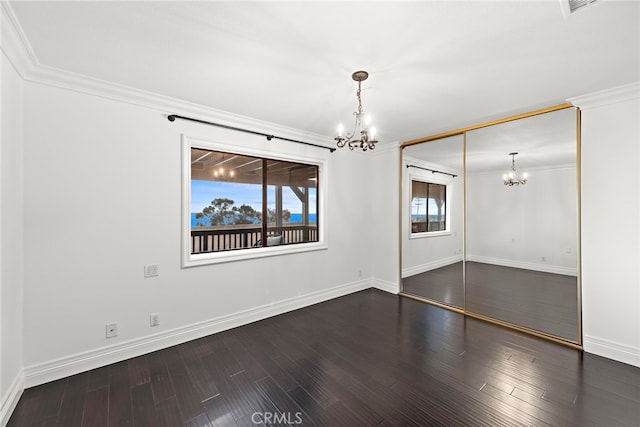 spare room with dark wood-type flooring, ornamental molding, and a notable chandelier