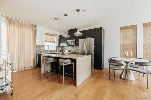 kitchen with decorative light fixtures, backsplash, a center island, light hardwood / wood-style flooring, and stainless steel appliances