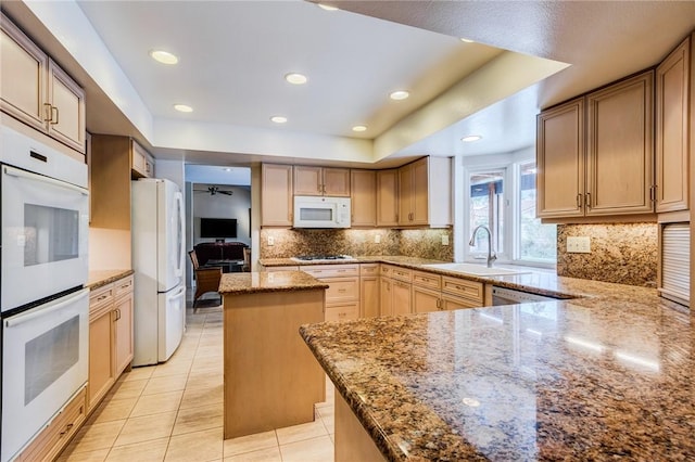 kitchen with light stone countertops, white appliances, a center island, and sink