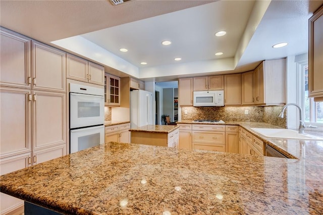 kitchen with a raised ceiling, sink, white appliances, and a center island