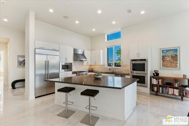 kitchen featuring a center island, built in appliances, wall chimney exhaust hood, white cabinets, and sink