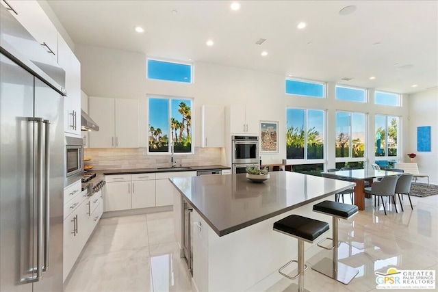 kitchen featuring exhaust hood, white cabinetry, stainless steel appliances, and a kitchen island