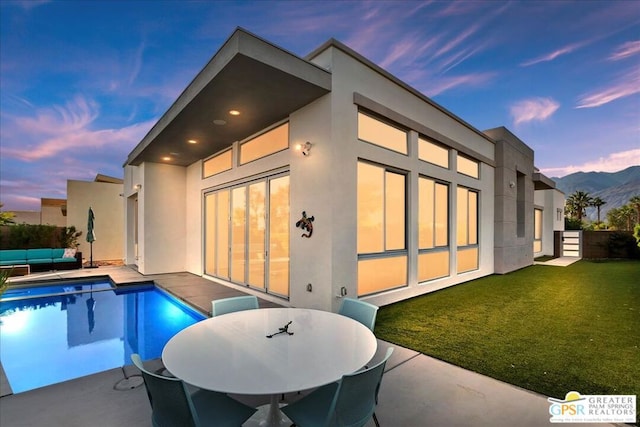 back house at dusk with a lawn and a patio area