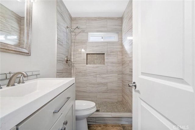 bathroom with toilet, vanity, and tiled shower