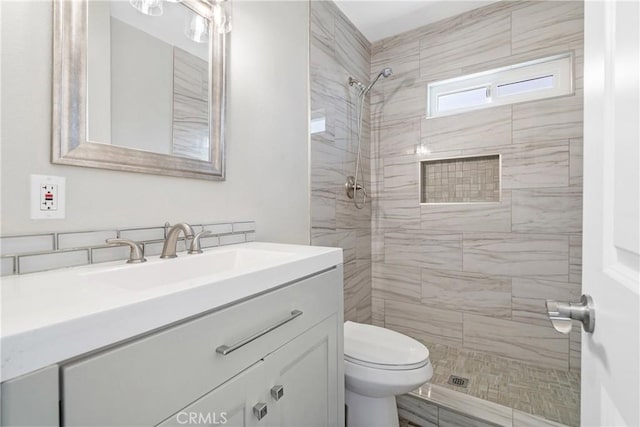 bathroom with toilet, tiled shower, and vanity