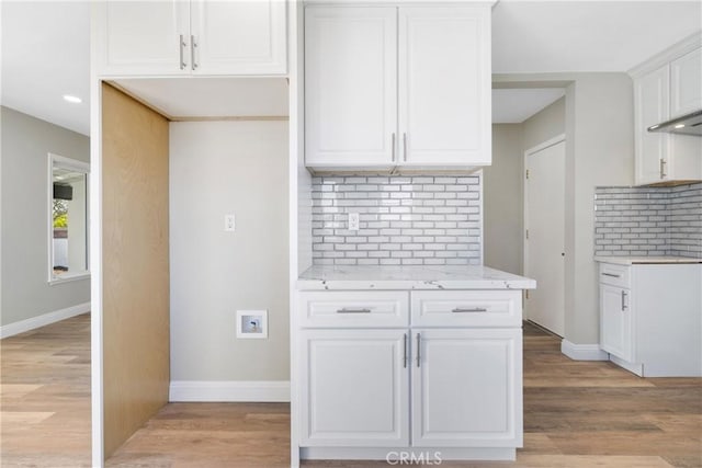 kitchen featuring white cabinetry, light stone countertops, backsplash, and light wood-type flooring