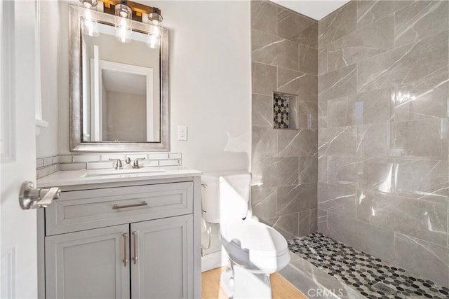 bathroom with toilet, a tile shower, and vanity