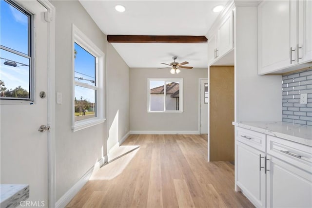 unfurnished dining area featuring ceiling fan, light hardwood / wood-style floors, and beamed ceiling