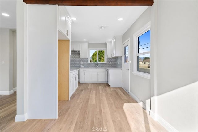 kitchen featuring backsplash, sink, light wood-type flooring, white cabinets, and beamed ceiling