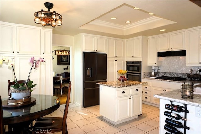 kitchen with a raised ceiling, a kitchen island, light stone counters, and black appliances