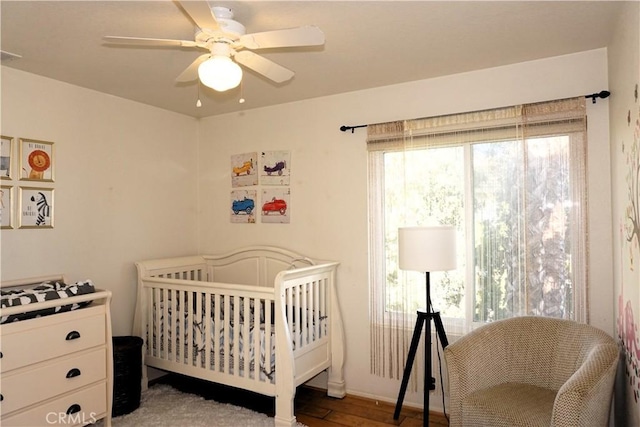 bedroom with a nursery area, ceiling fan, and hardwood / wood-style flooring