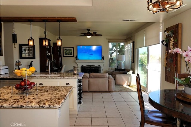 kitchen featuring white cabinetry, a center island with sink, light tile patterned floors, pendant lighting, and light stone countertops