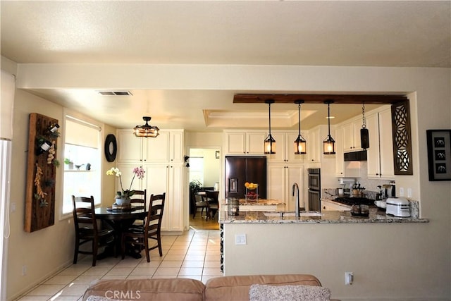 kitchen featuring kitchen peninsula, white cabinets, pendant lighting, light stone countertops, and black appliances