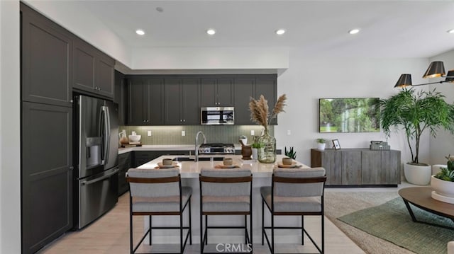 kitchen with stainless steel appliances, an island with sink, a kitchen breakfast bar, backsplash, and sink