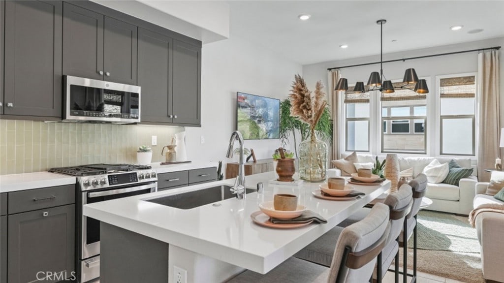 kitchen featuring appliances with stainless steel finishes, a kitchen island with sink, pendant lighting, a breakfast bar, and sink