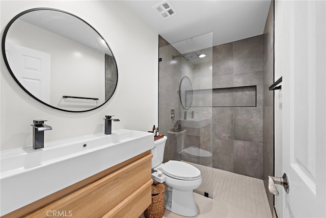 bathroom featuring toilet, vanity, tile patterned flooring, and tiled shower