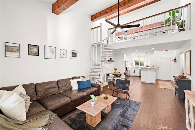 living room with ceiling fan, a towering ceiling, beamed ceiling, and hardwood / wood-style flooring