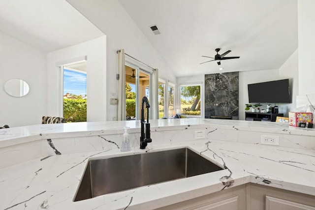 kitchen featuring lofted ceiling, ceiling fan, light stone countertops, and sink