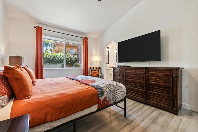 bedroom with light hardwood / wood-style floors, ensuite bathroom, and lofted ceiling