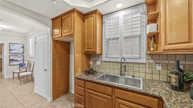 kitchen featuring dark stone counters, sink, backsplash, ornamental molding, and light tile patterned floors