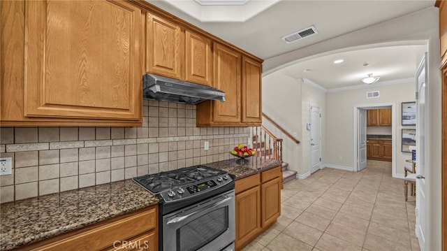 kitchen with light tile patterned floors, stainless steel gas range oven, dark stone counters, and crown molding