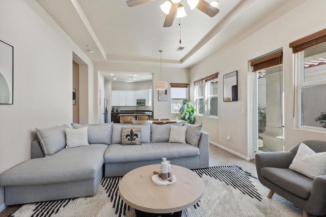 tiled living room with ceiling fan and a tray ceiling