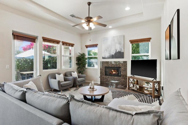 living room with ceiling fan, a high end fireplace, and a raised ceiling