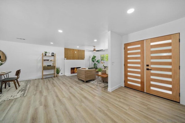 entryway with ceiling fan, a fireplace, and light hardwood / wood-style floors