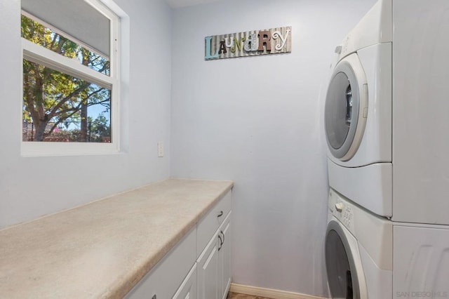 clothes washing area with stacked washer and clothes dryer and cabinets