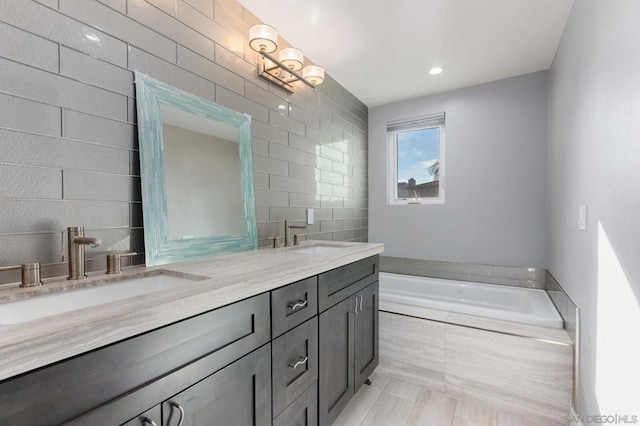 bathroom with a relaxing tiled tub, vanity, and tile patterned flooring