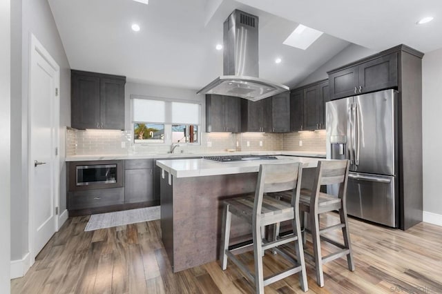 kitchen with vaulted ceiling with skylight, light hardwood / wood-style floors, a kitchen island, island exhaust hood, and stainless steel appliances