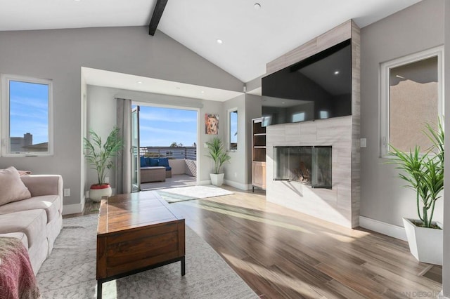 living room featuring vaulted ceiling with beams, light wood-type flooring, and a large fireplace