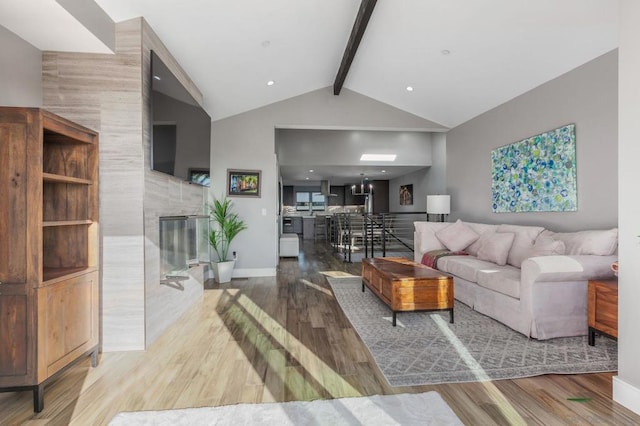 living room featuring wood-type flooring, a tile fireplace, and lofted ceiling with beams