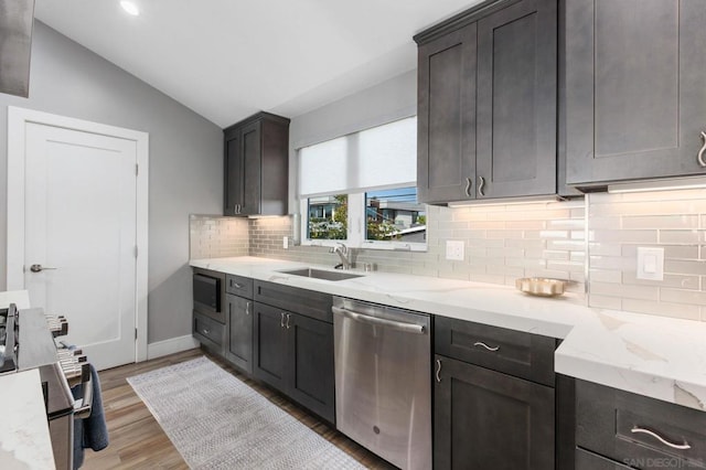 kitchen with dishwasher, light stone countertops, vaulted ceiling, light hardwood / wood-style flooring, and sink