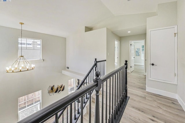 corridor featuring an inviting chandelier, lofted ceiling, light hardwood / wood-style floors, and a wealth of natural light