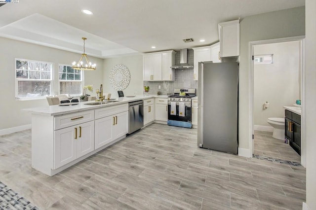 kitchen with appliances with stainless steel finishes, white cabinetry, sink, kitchen peninsula, and wall chimney exhaust hood