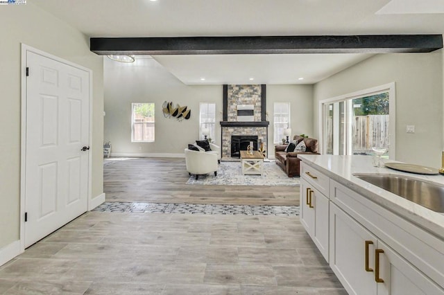 kitchen featuring white cabinetry, beam ceiling, a stone fireplace, and light hardwood / wood-style flooring