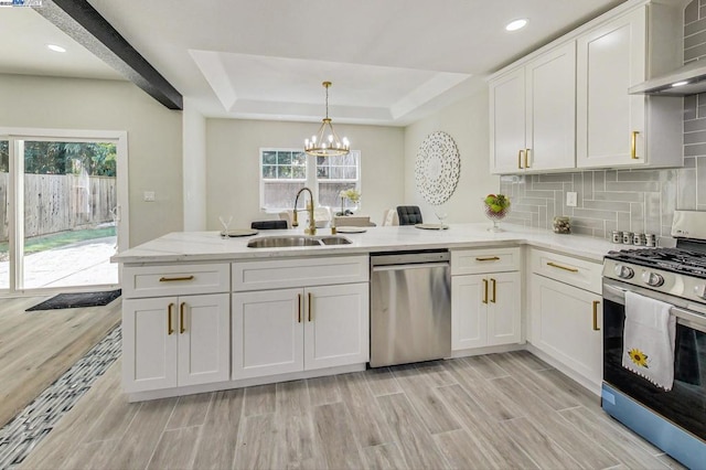 kitchen with sink, white cabinets, hanging light fixtures, stainless steel appliances, and wall chimney exhaust hood