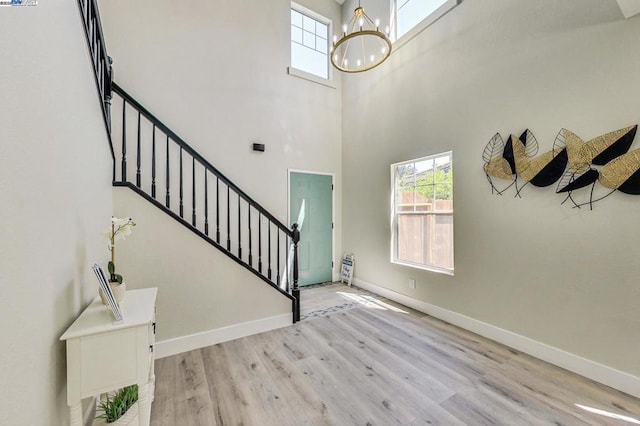 entryway with a towering ceiling, a chandelier, and light hardwood / wood-style flooring