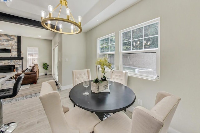 dining room featuring a notable chandelier, light hardwood / wood-style floors, a large fireplace, and beamed ceiling