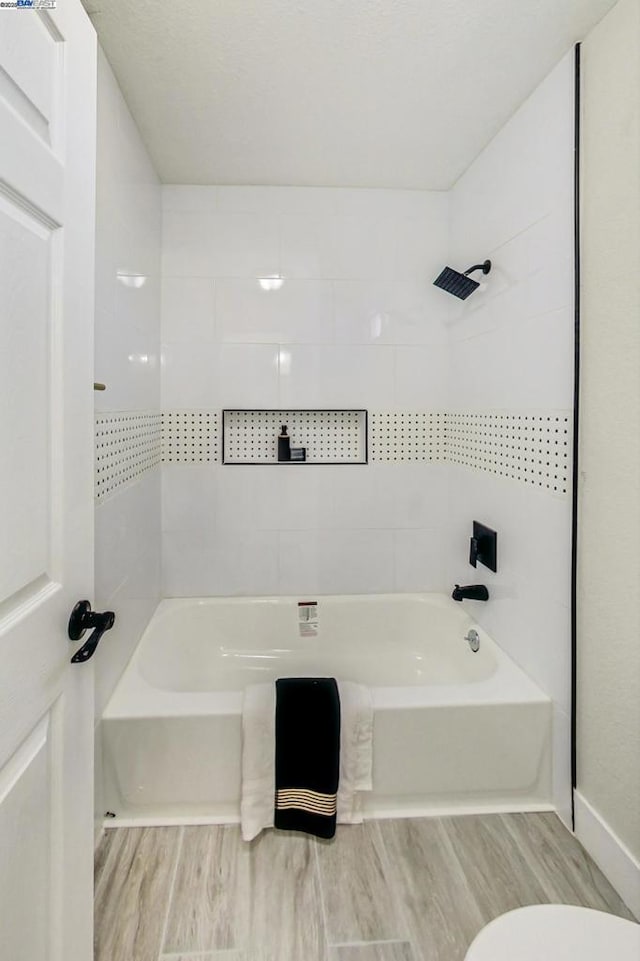 bathroom with tiled shower / bath, wood-type flooring, and toilet