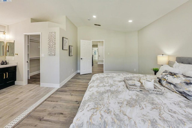 bedroom featuring lofted ceiling, a walk in closet, and light hardwood / wood-style floors