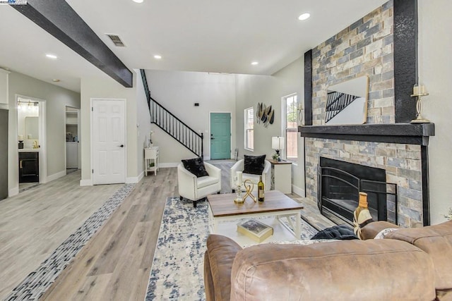 living room featuring beamed ceiling, a large fireplace, and light hardwood / wood-style flooring