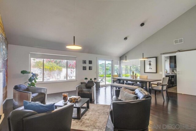 living room with a barn door, hardwood / wood-style floors, and high vaulted ceiling