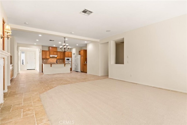 unfurnished living room featuring light colored carpet and a chandelier