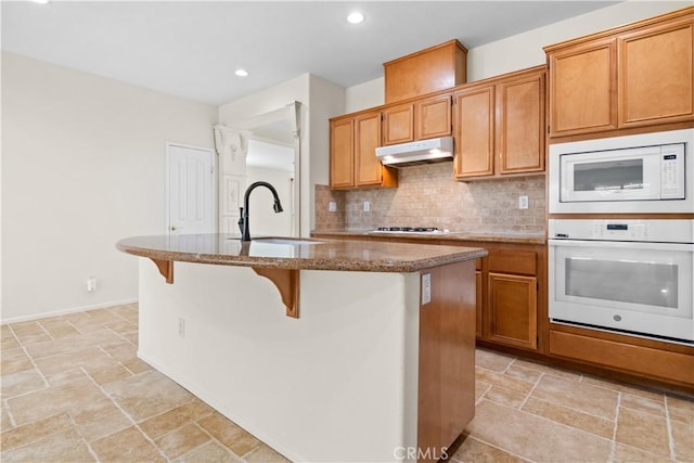 kitchen with sink, tasteful backsplash, a kitchen breakfast bar, white appliances, and a kitchen island with sink